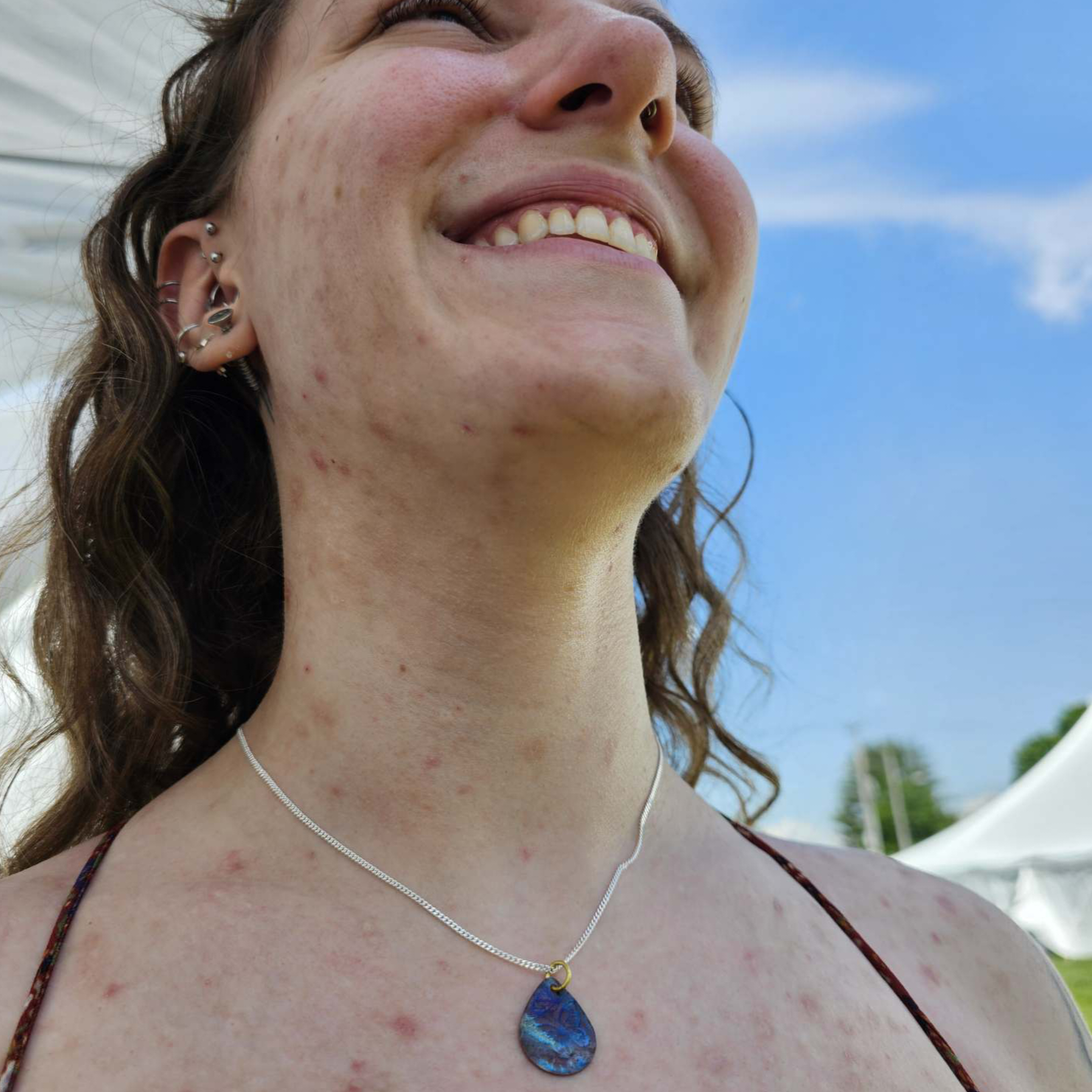 Smiling girl looking upwards with silver chain and flame painted copper pendant around her neck