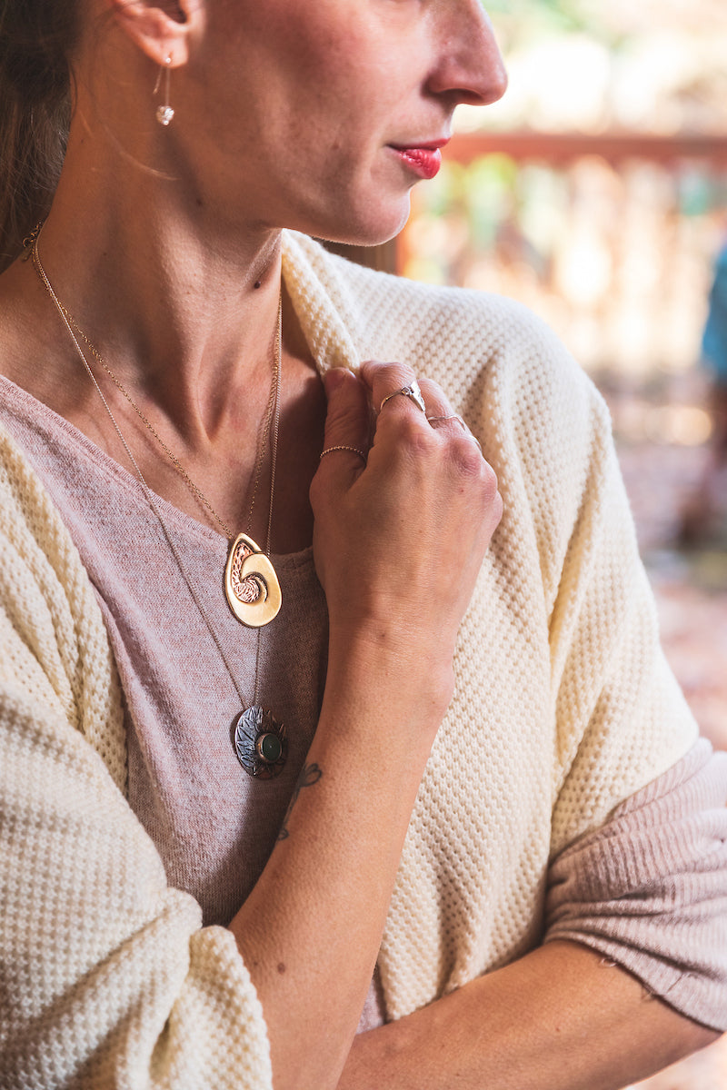 a woman wearing two pendant necklaces and a pair of drop earrings.