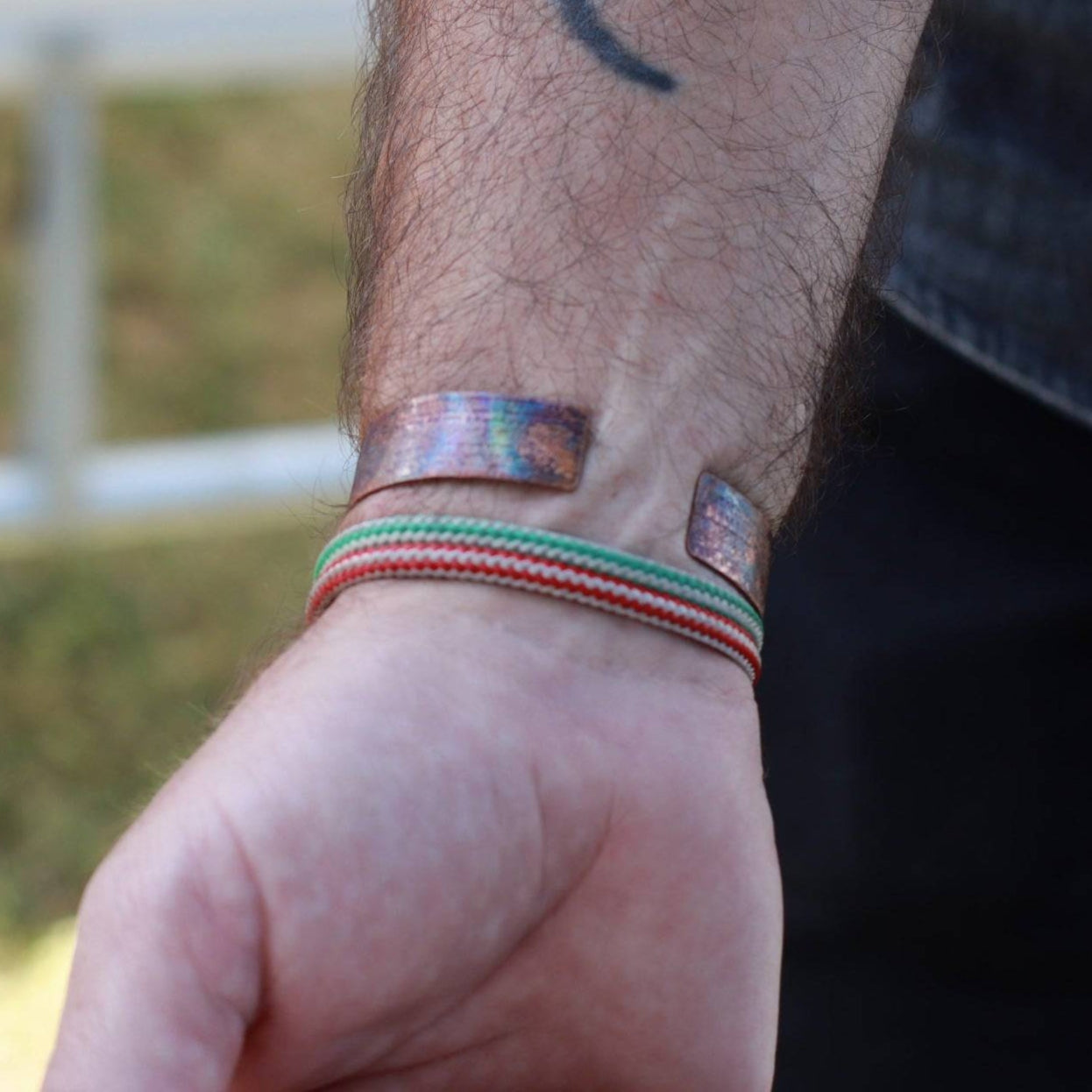 the back of a handmade flame painted copper cuff bracelets modeled on man's wrist