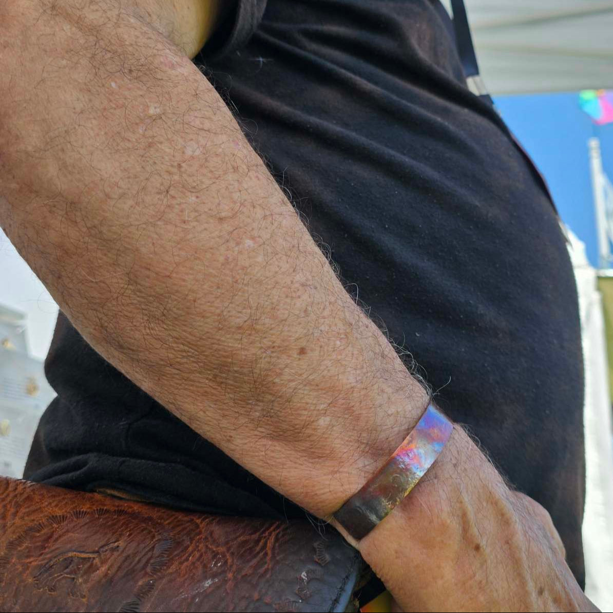 Man with black shirt and brown leather bag wearing a flame painted copper cuff bracelet