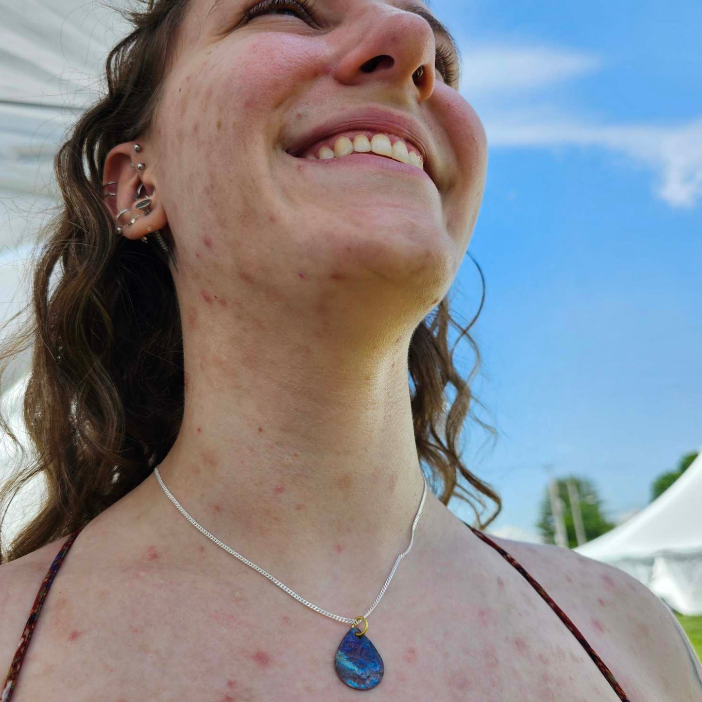 Flame Painted Copper Pendant with silver chain worn around smiling woman's neck.