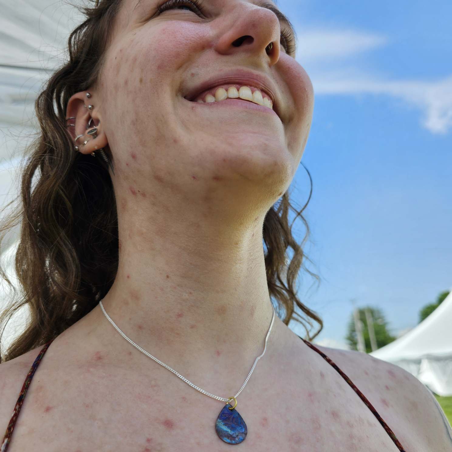 Flame Painted Copper Pendant with silver chain worn around smiling woman's neck.