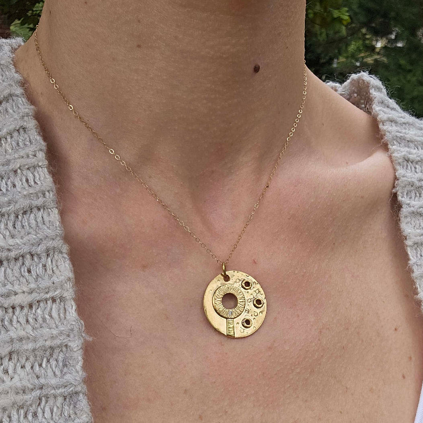 Woman with grey sweater wearing a Gold circle necklace with symbols of a bubble wand and bubbles.