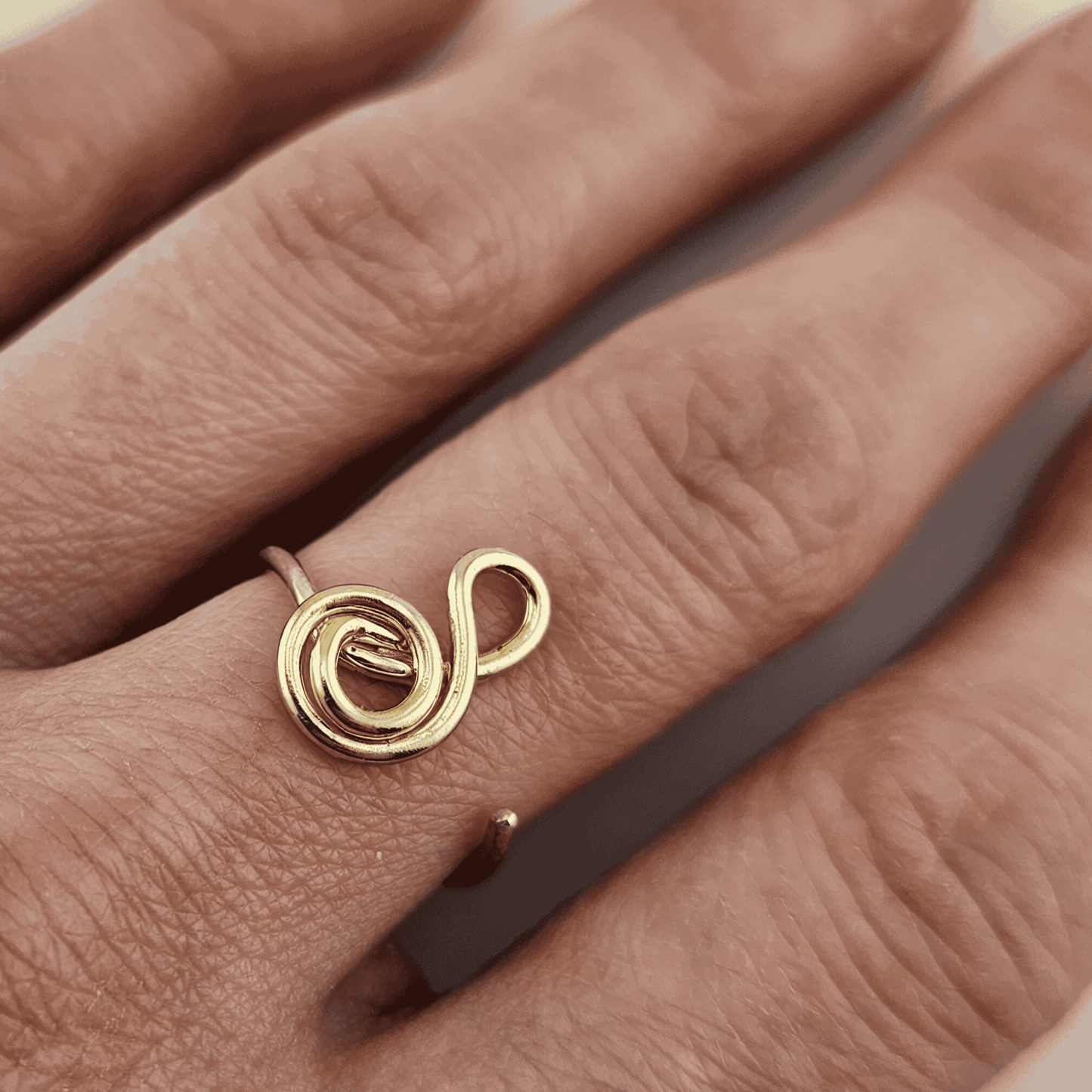 A woman's hand wearing a gold adjustable gratitude ring on her middle finger.