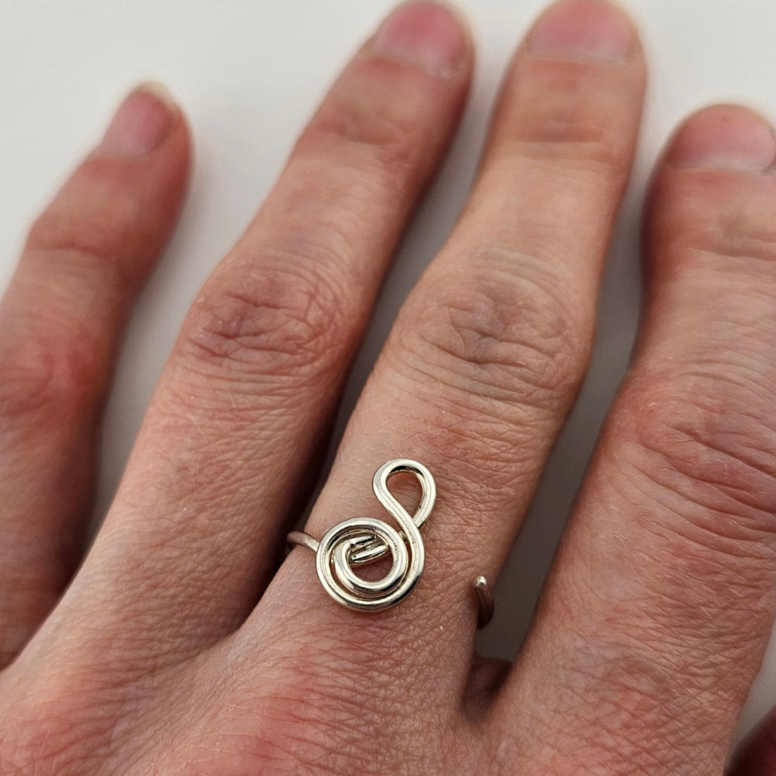 A woman's hand wearing a silver adjustable gratitude ring on her middle finger.