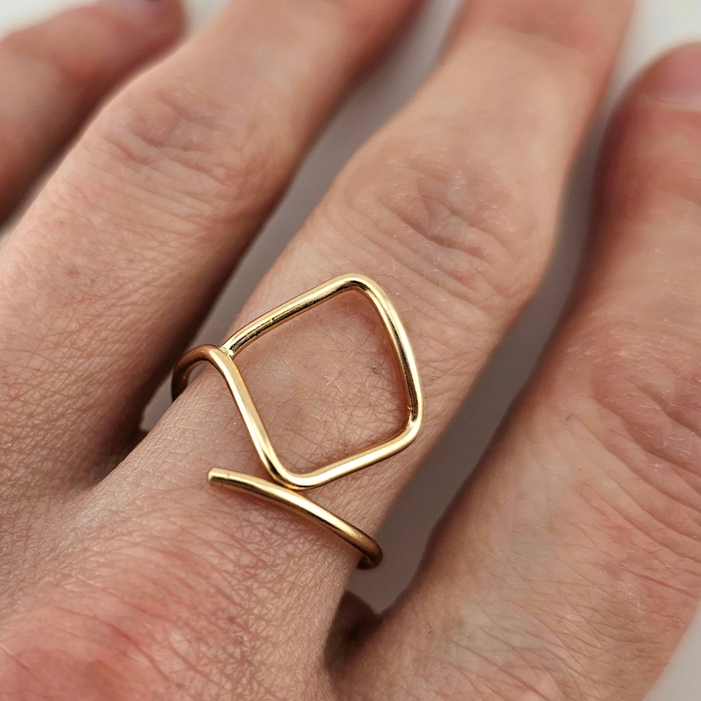 Adjustable Gold square wire ring worn on woman's finger. 