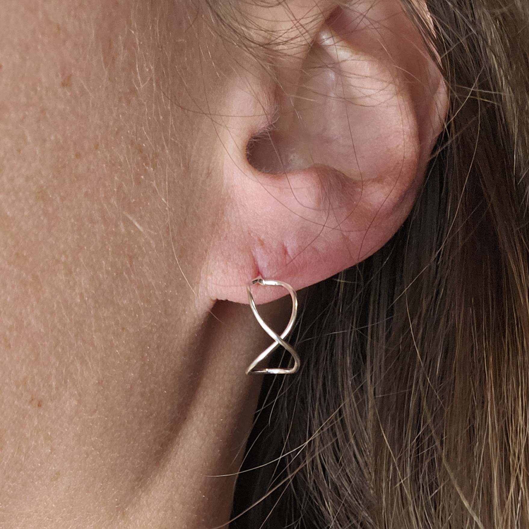 Silver infinity shaped earring worn on a woman's earlobe.