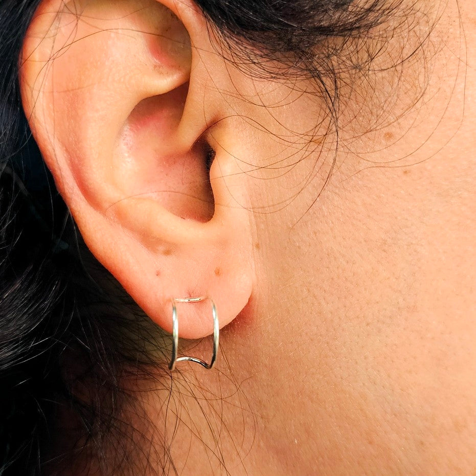 Close up of silver half hoop style earrings on woman's ear. 