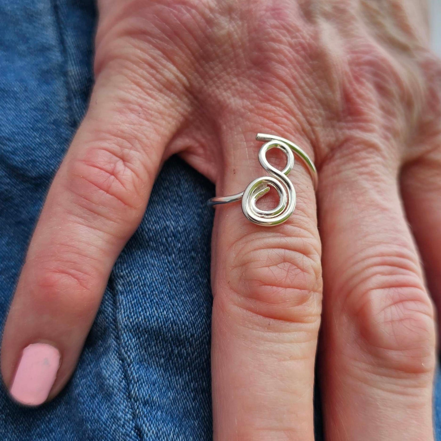 Silver adjustable gratitude ring worn on woman's index finger placed on jean pants.