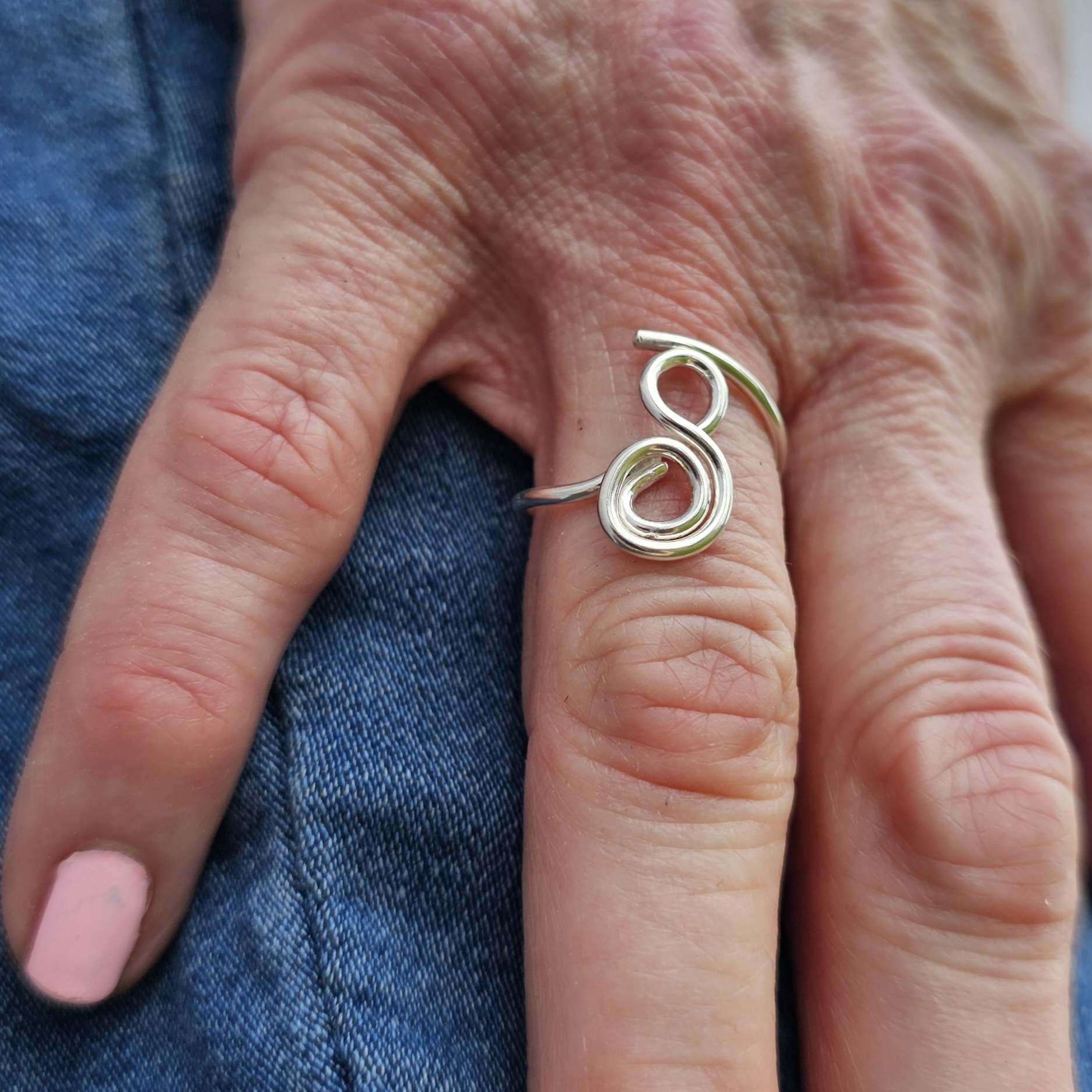 Silver adjustable gratitude ring worn on woman's index finger placed on jean pants.