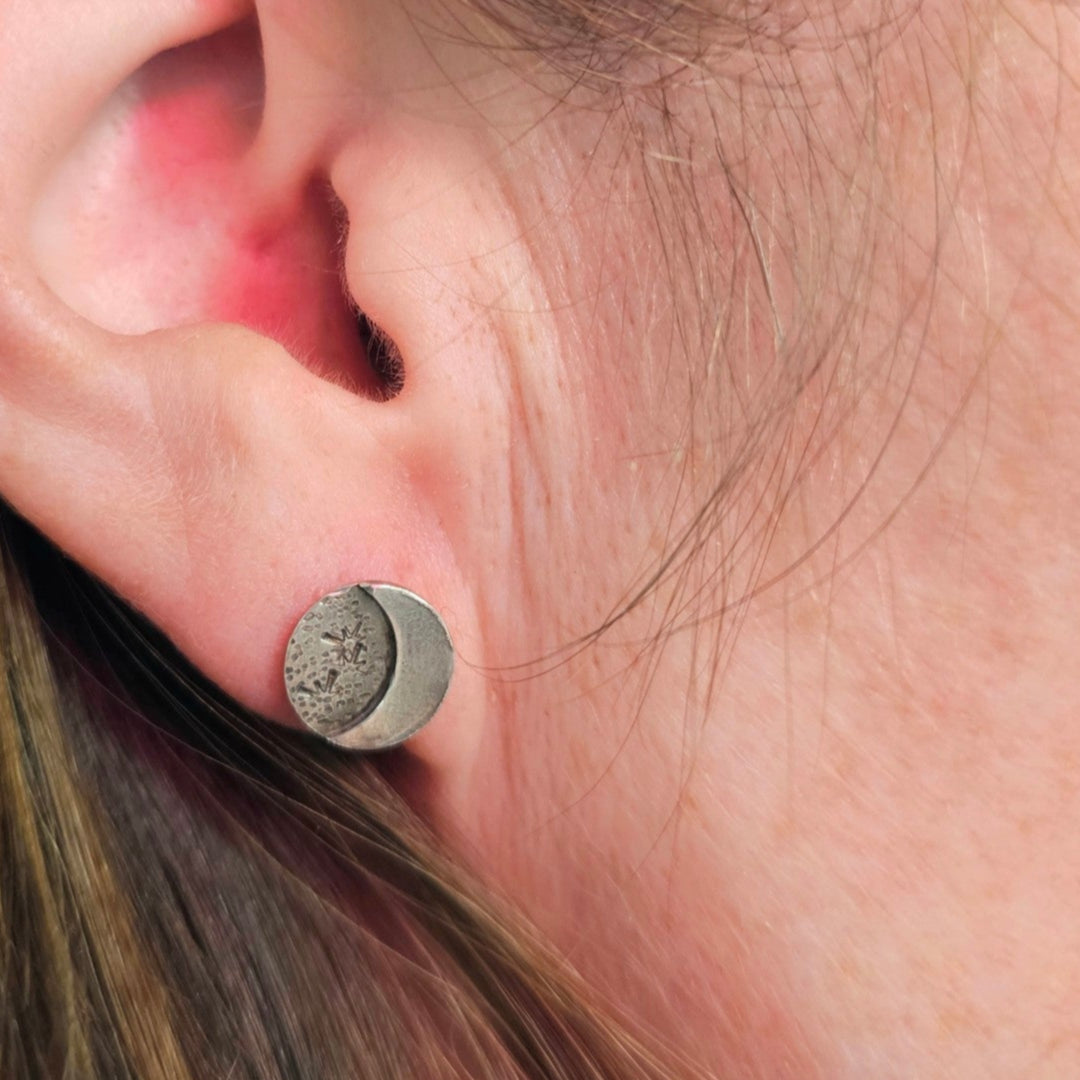 Close up of silver star and moon stud earring on woman's ear.