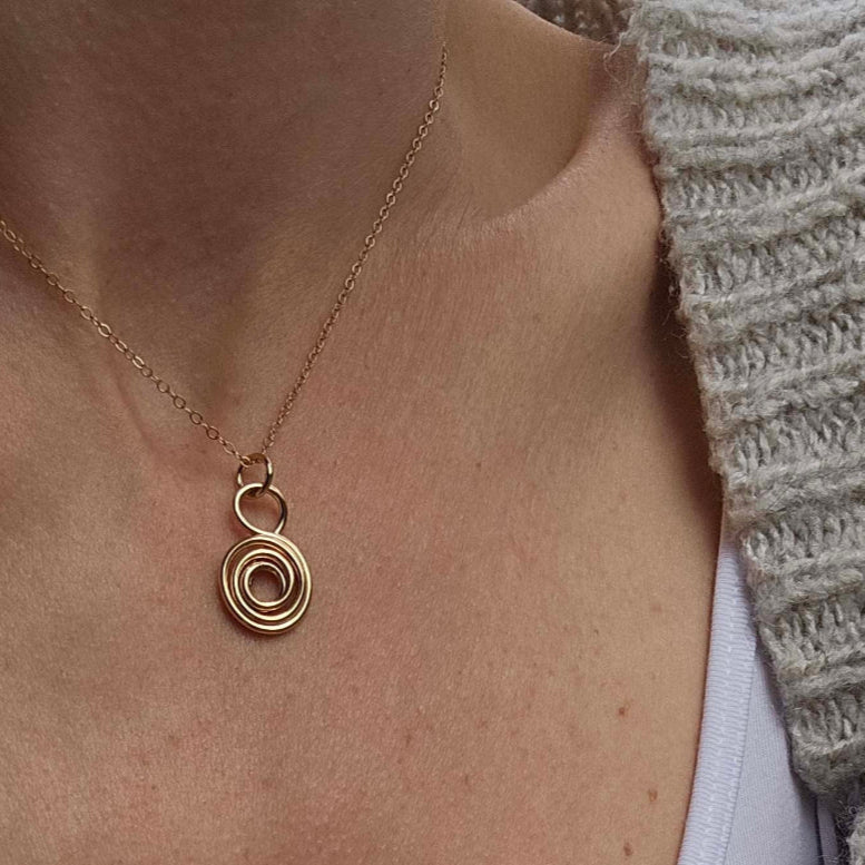 Woman with sweater wearing 14K Gold love and gratitude symbol necklace.