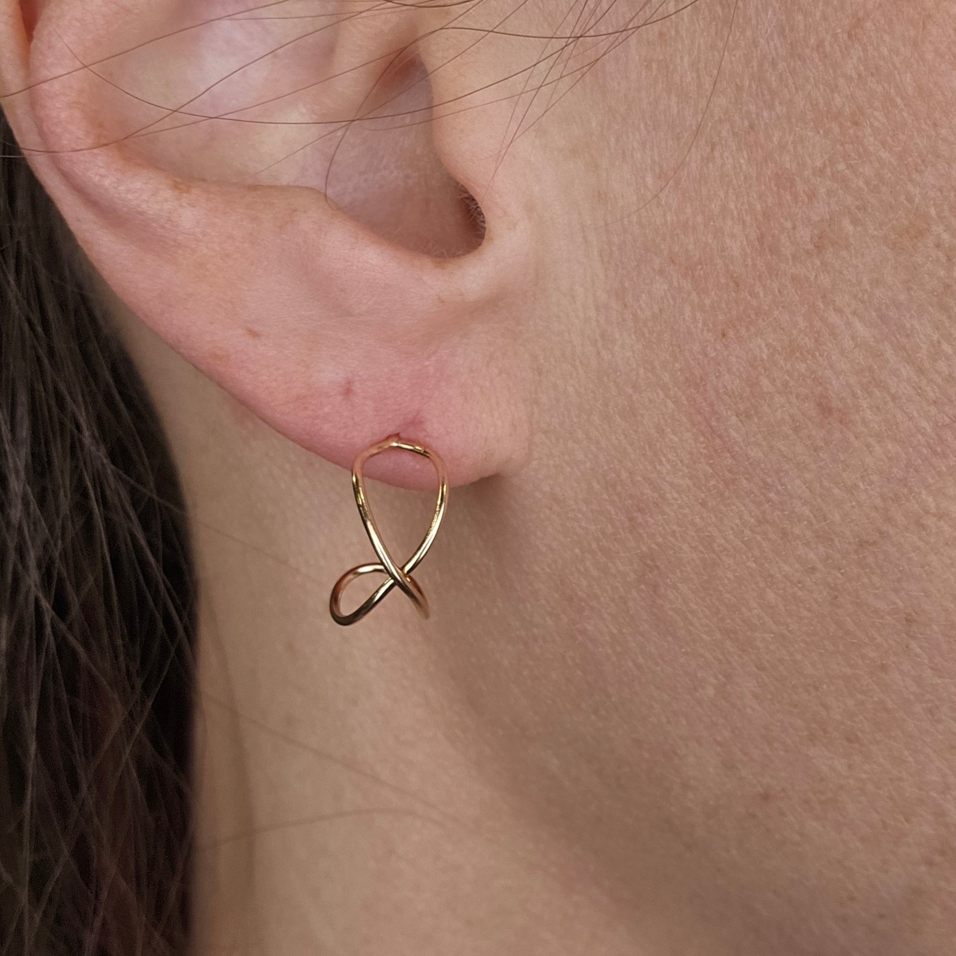 Woman wearing gold infinity earrings in her earlobe.