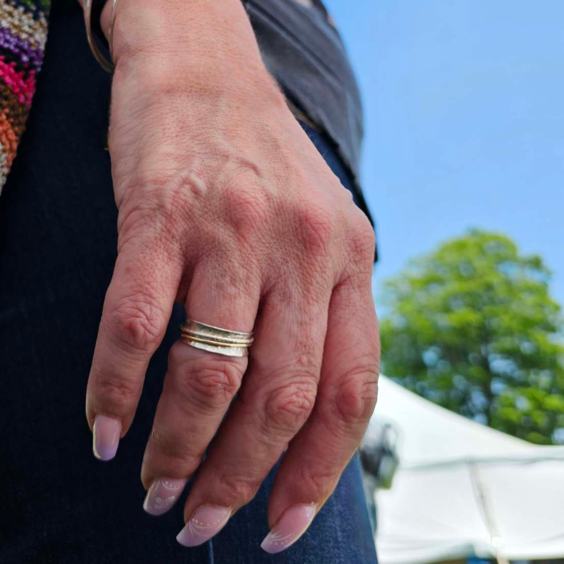 Woman wearing silver and gold anxiety ring spinner on her index finger.