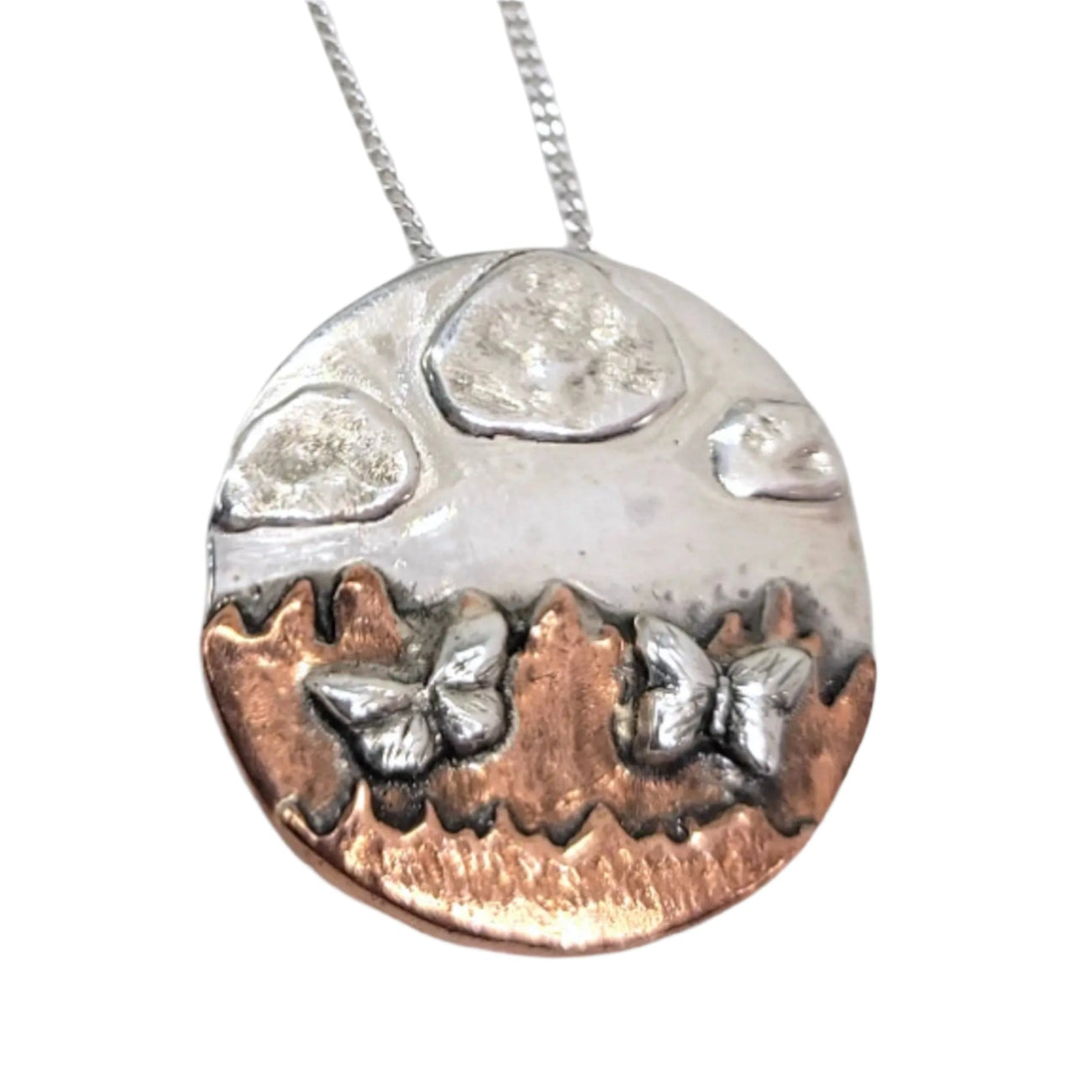 Necklace in silver and copper of a mountainscape with butterflies and clouds.