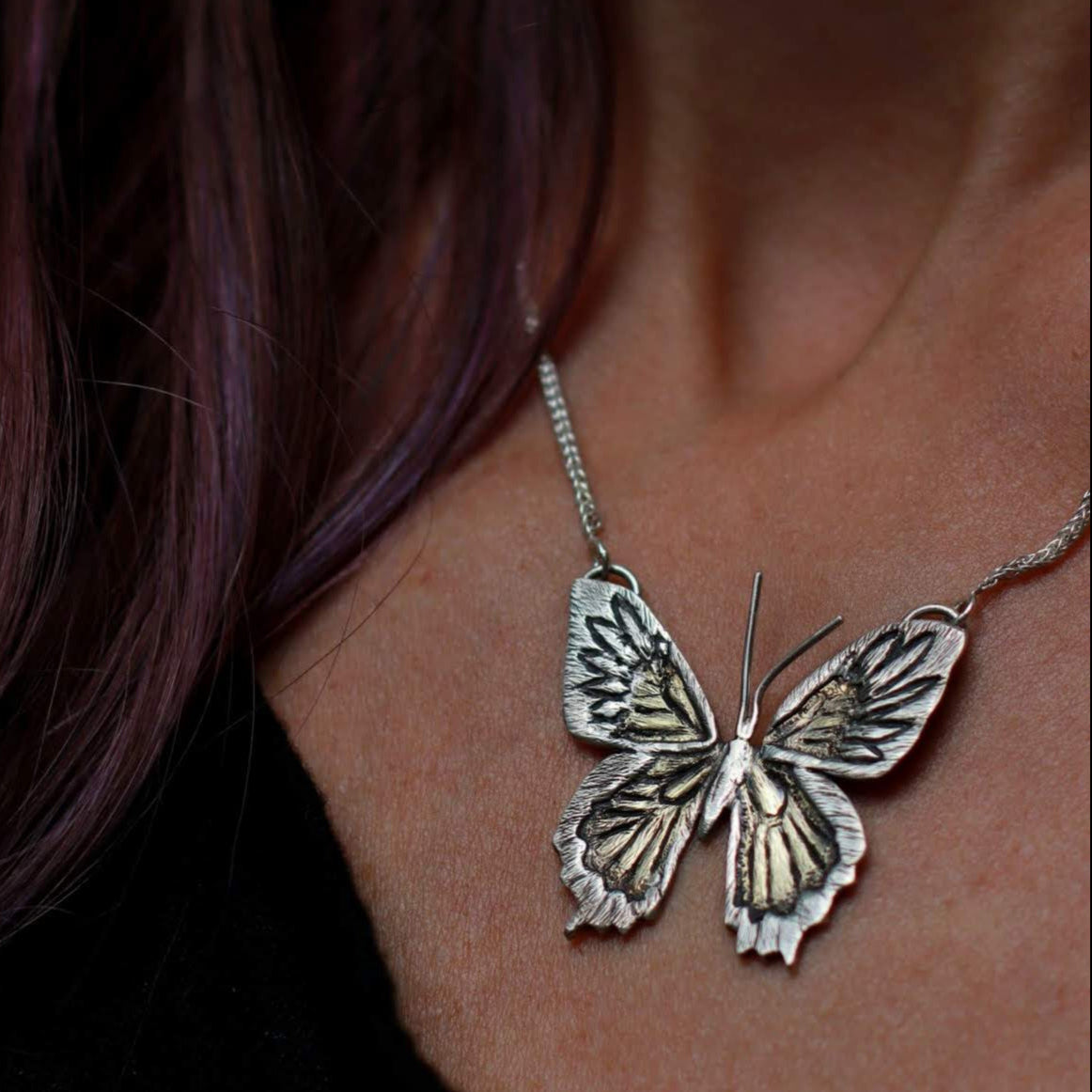 close up of handmade butterfly pendant necklace on woman's neck with black shirt.