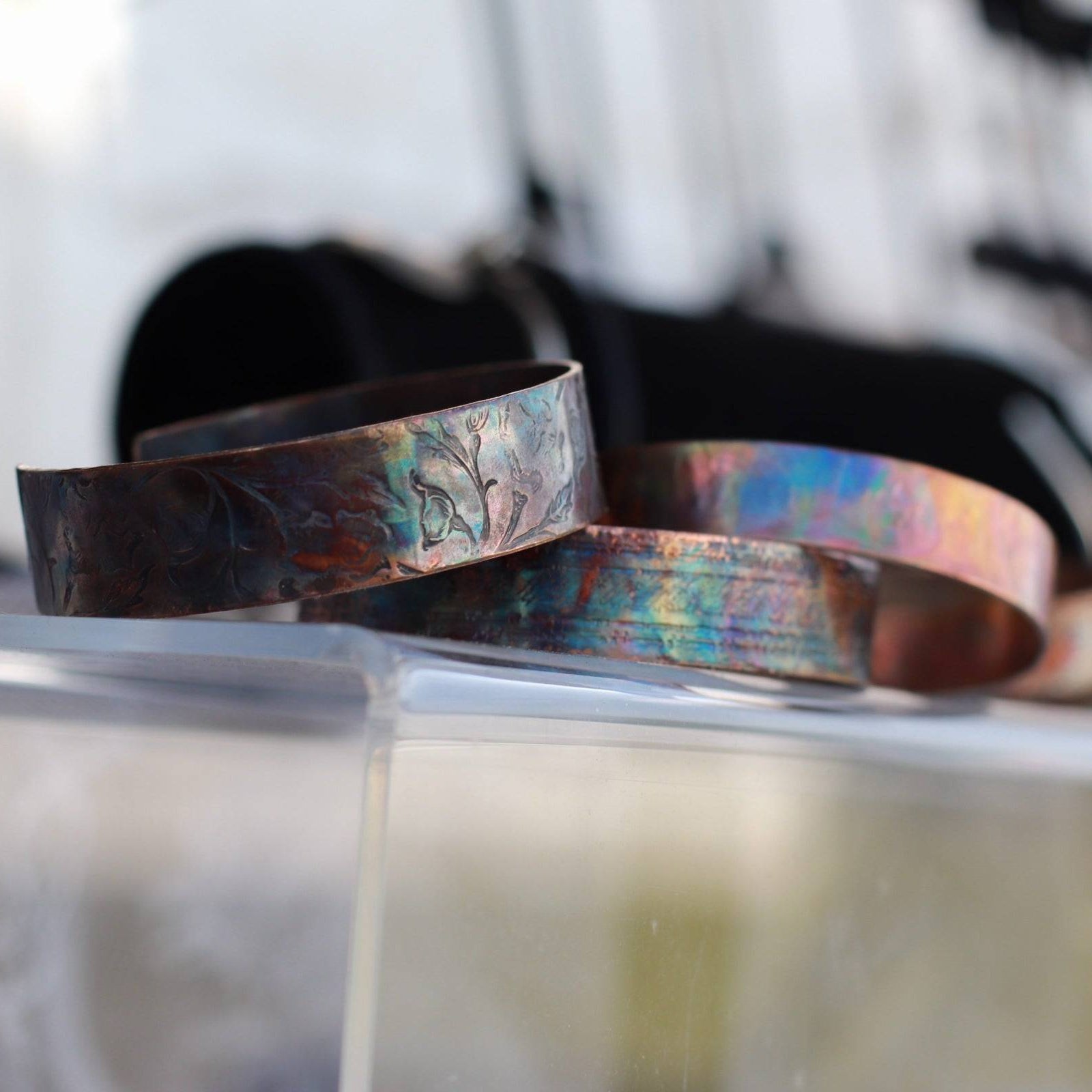 flame painted copper cuff bracelets on a clear acrylic display.