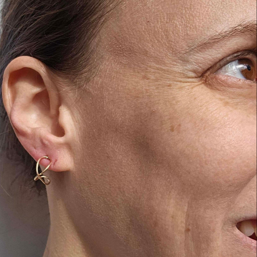 Gold Infinity earrings worn on woman's ear.