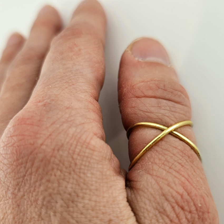 A woman's hand wearing a 14K gold infinity ring on her middle finger.