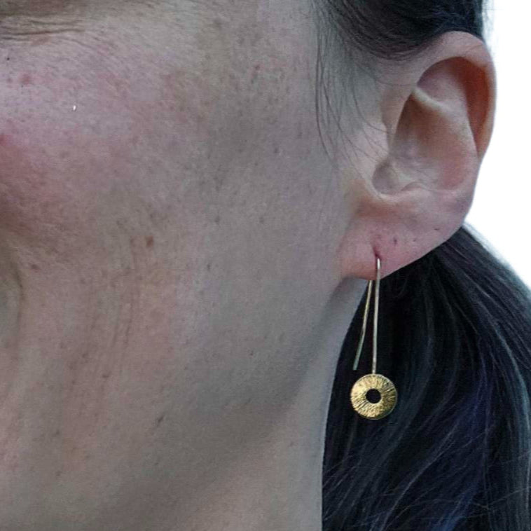 Smiling woman with ponytail wearing gold drop manifestation earrings.