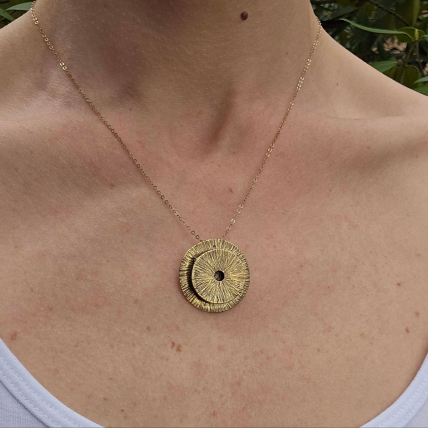 a woman wearing a gold manifestation pendant necklace