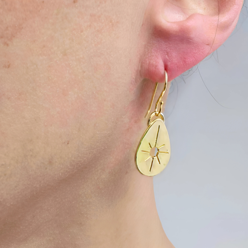 Close up of woman's ear wearing a drop gold earring.