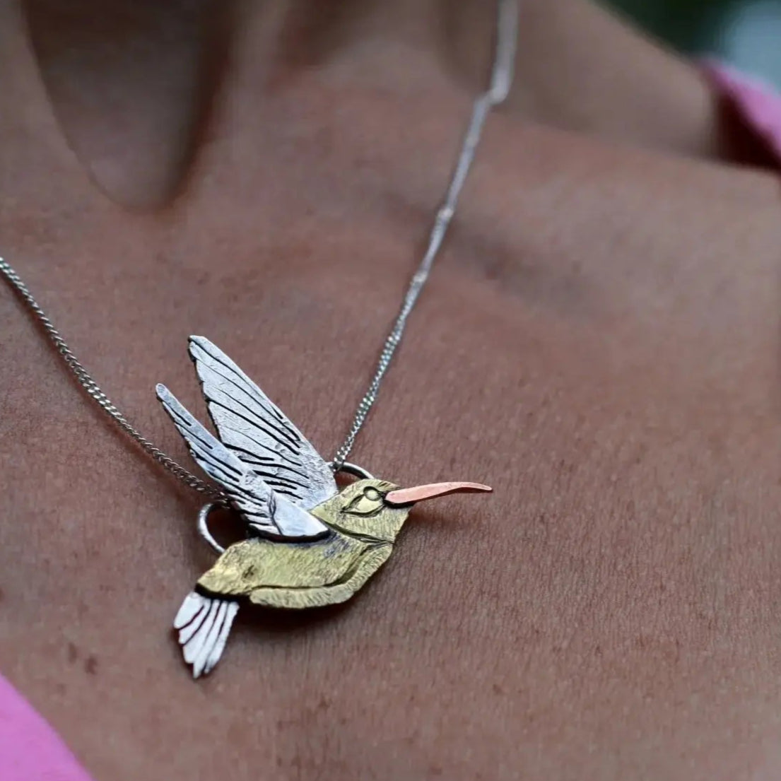 Handmade hummingbird necklace worn around a woman's neck with a pink shirt peeking out on the sides.