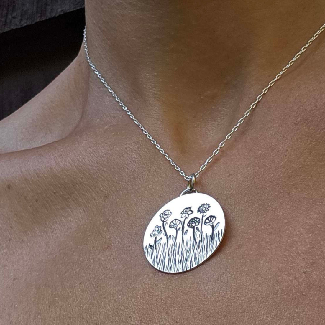 Silver necklace with birth month flowers made into a garden worn on a woman's neck.