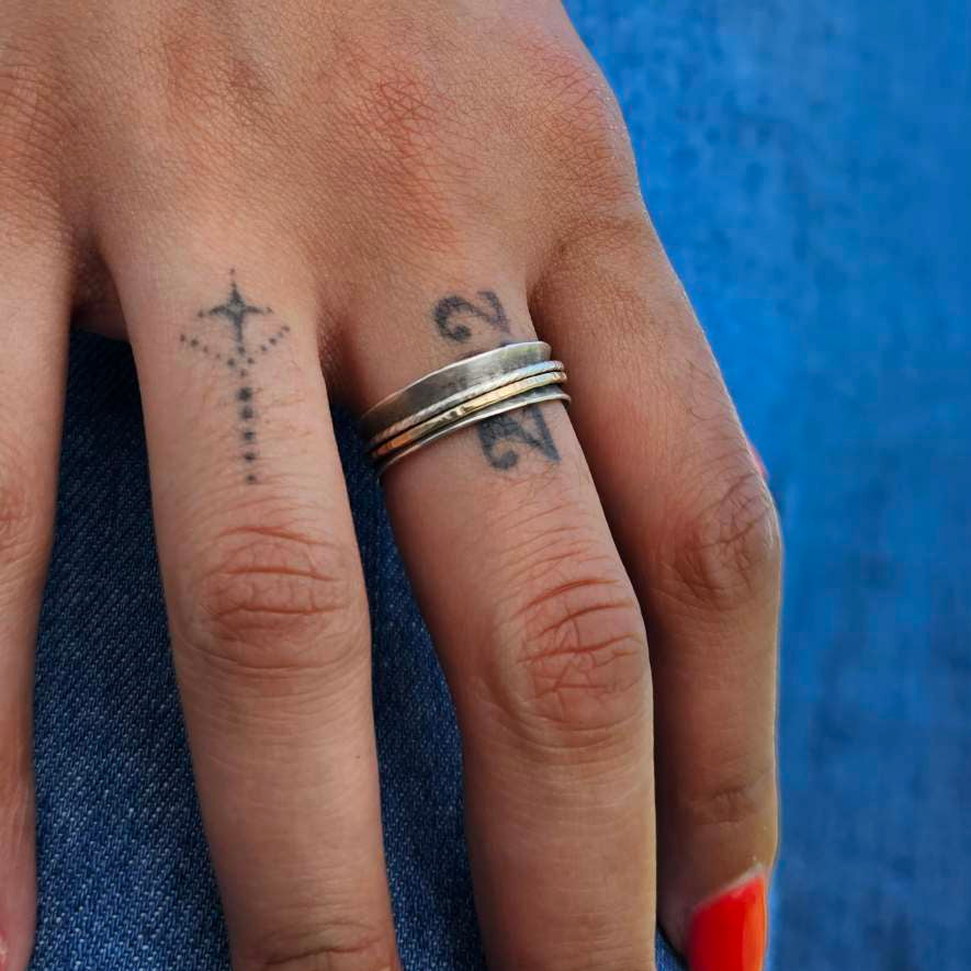 Woman wearing blue jeans with finger tattoos wearing a silver presence anxiety spinner ring.