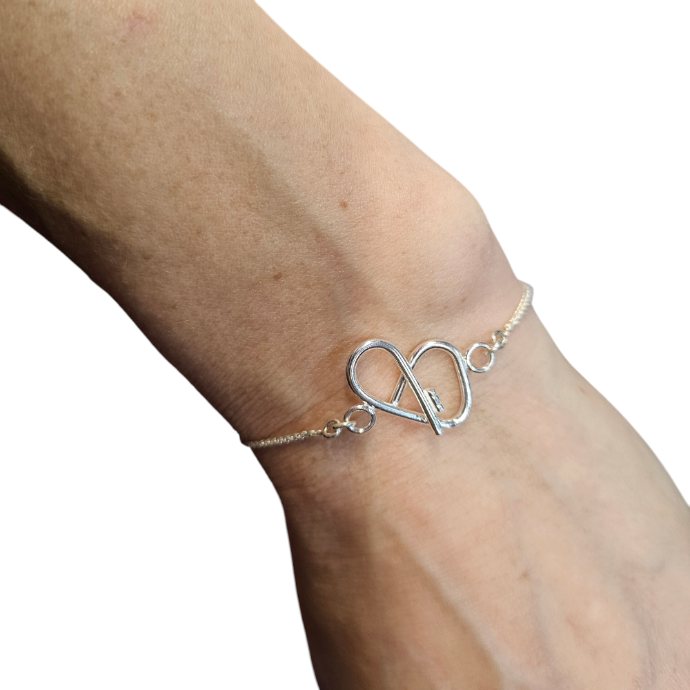 Close up of a silver heart shaped bracelet on change on a woman's wrist.