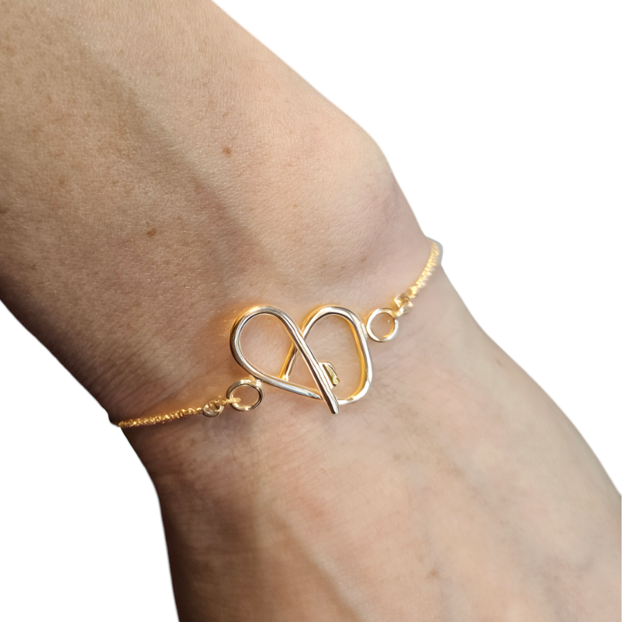 Close up of a gold heart shaped bracelet on change on a woman's wrist.