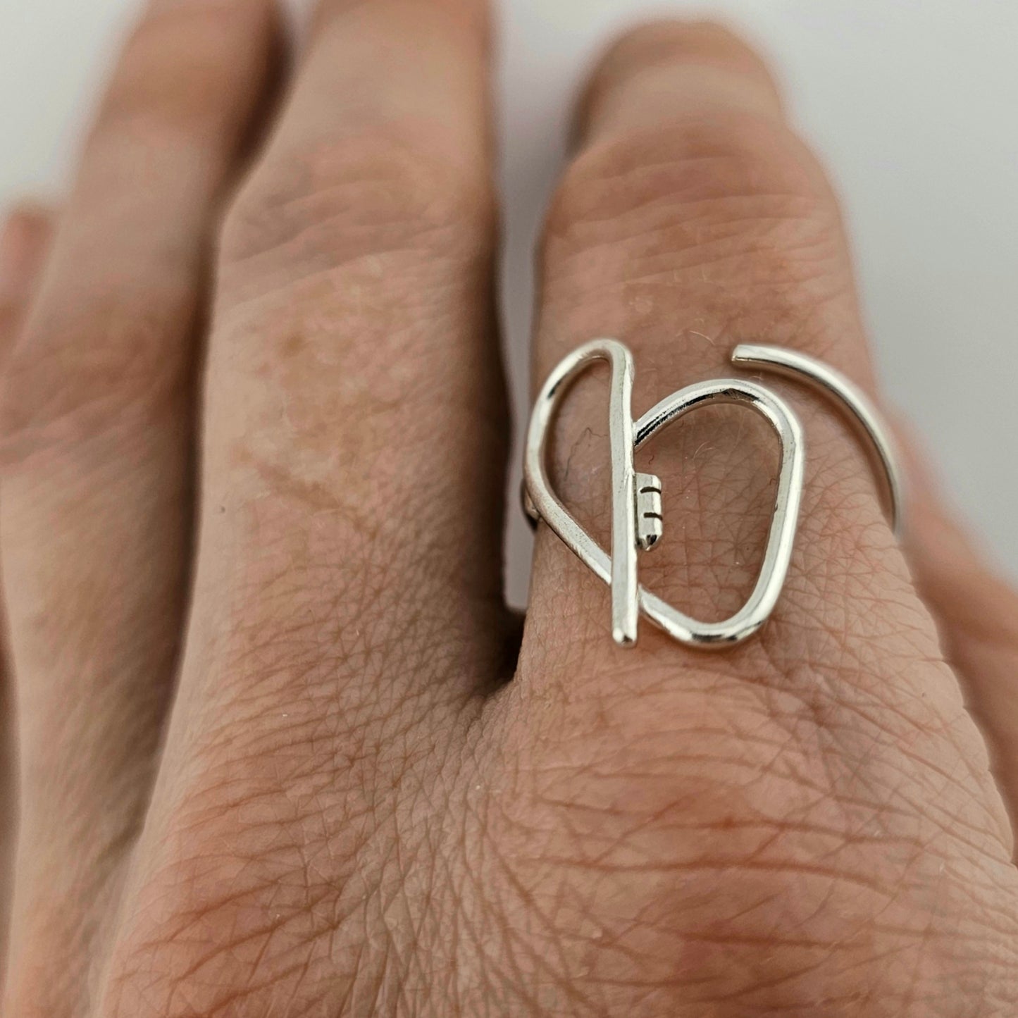 Woman's hand with a silver heart ring with a key in the middle on her pointer finger.