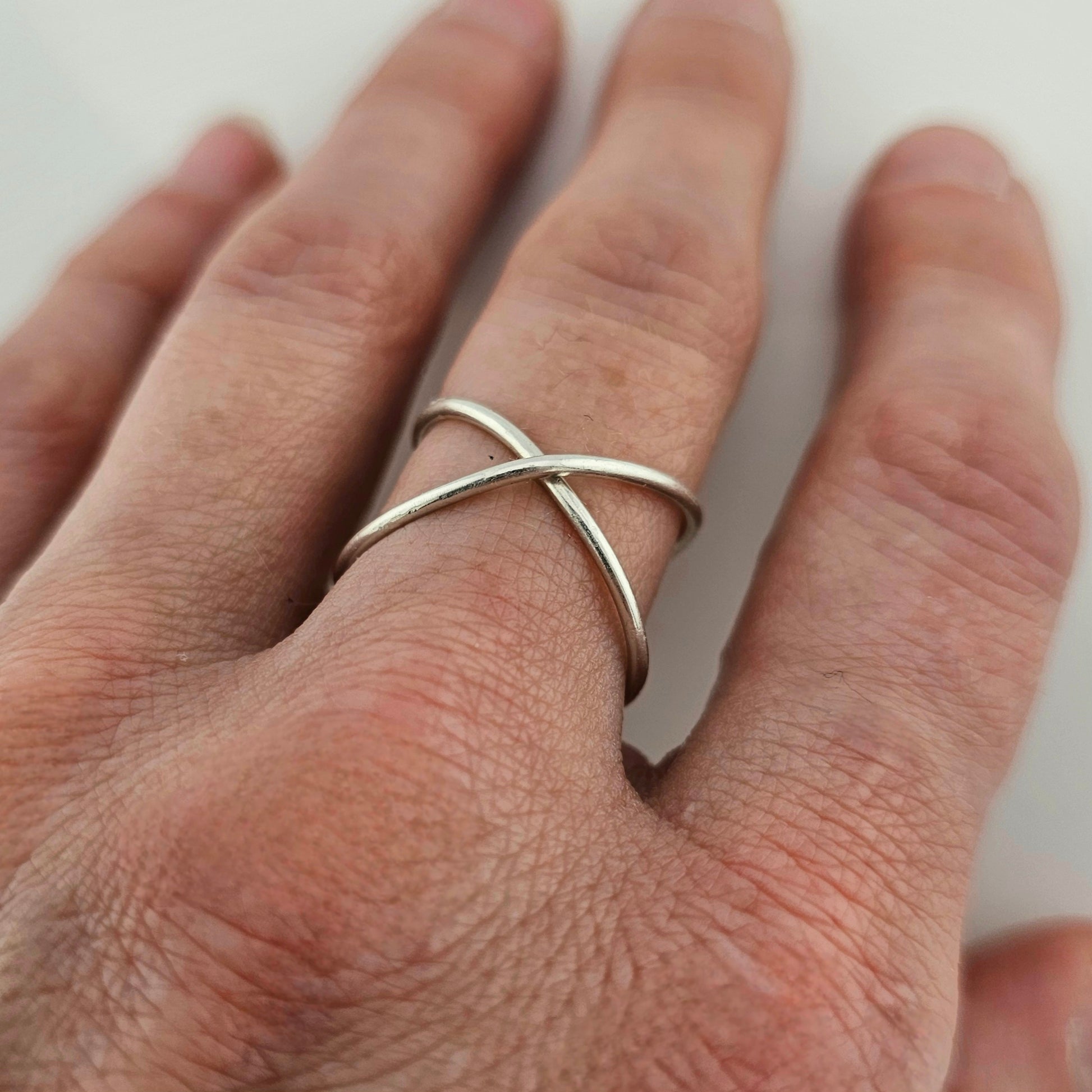 A woman's hand wearing a sterling silver infinity ring on her middle finger.