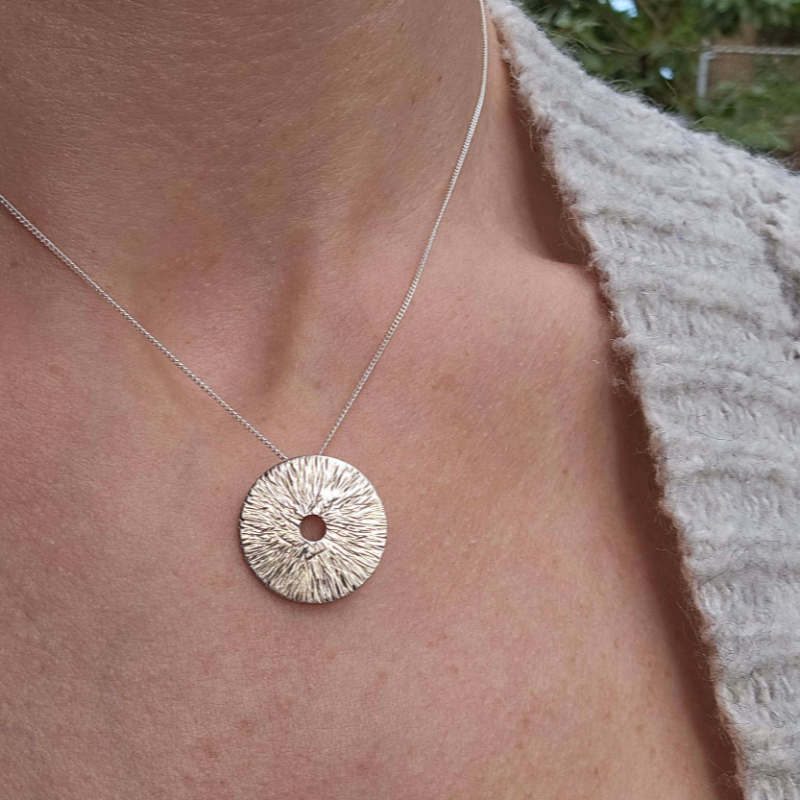 Silver manifestation necklace around a woman's neck with grey sweater.