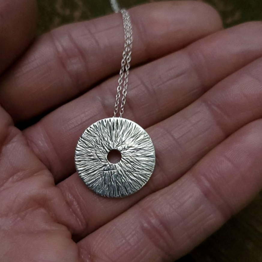 Handmade silver necklace for manifestation in a woman's hand.