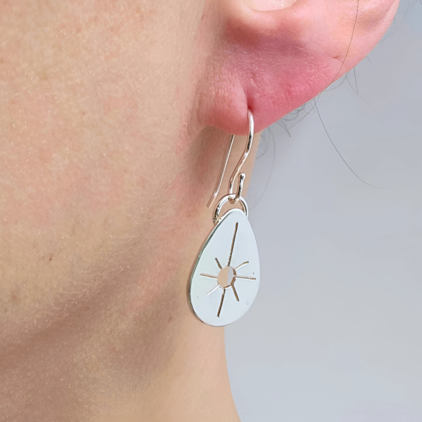 Close up of woman's ear wearing a drop silver earring.