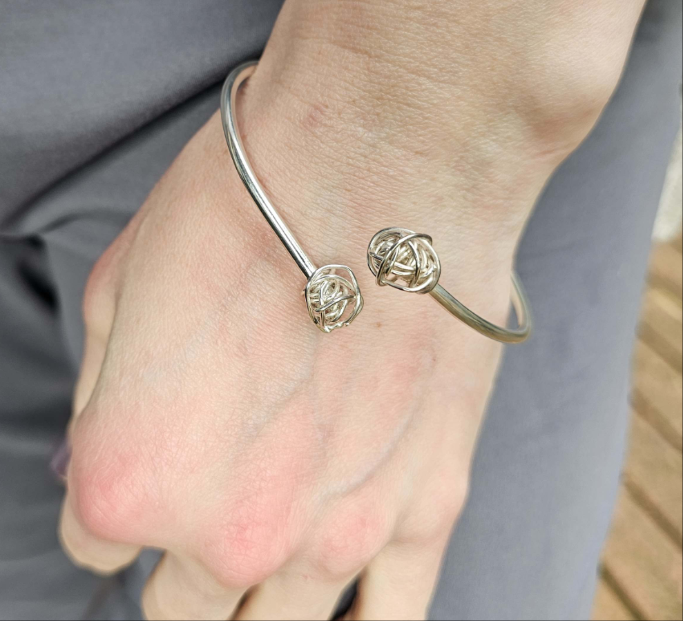 Woman's wrist adorned with a silver cuff bracelet with wire knots on either end.