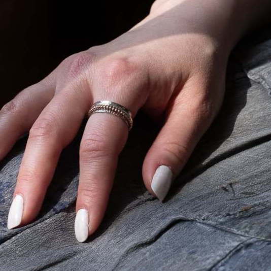 Woman's hand on her lap with white nail polish wearing silver spinner fidget ring.