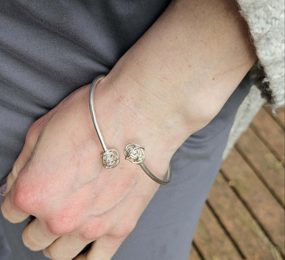 Woman's arm wearing a silver bracelet with knots at either end around her wrist.