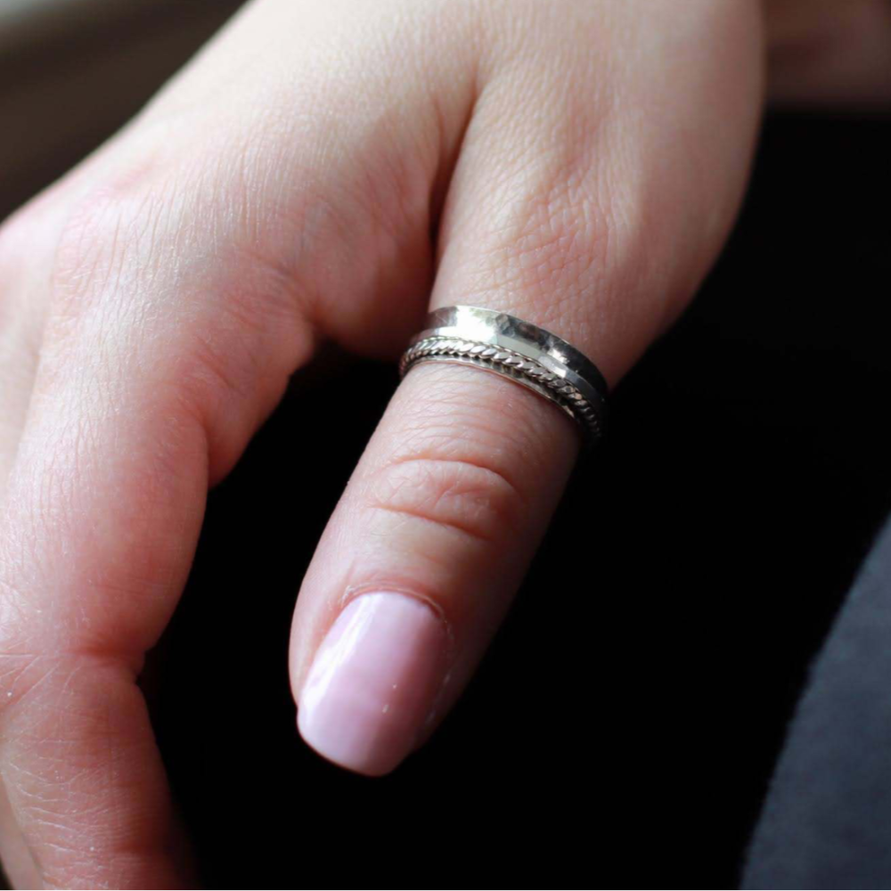 Woman's hand wearing silver spinner anxiety ring on her thumb.