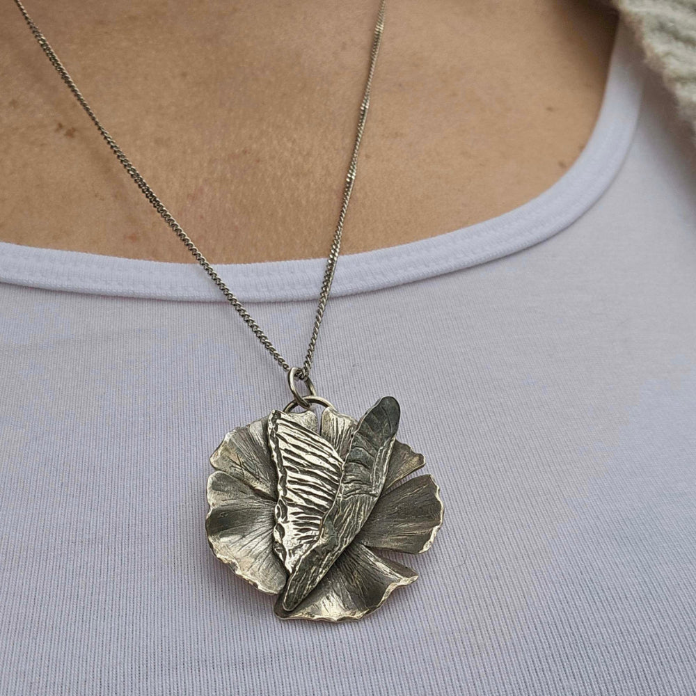 Handmade butterfly necklace with flower in silver on woman's neck atop white shirt.