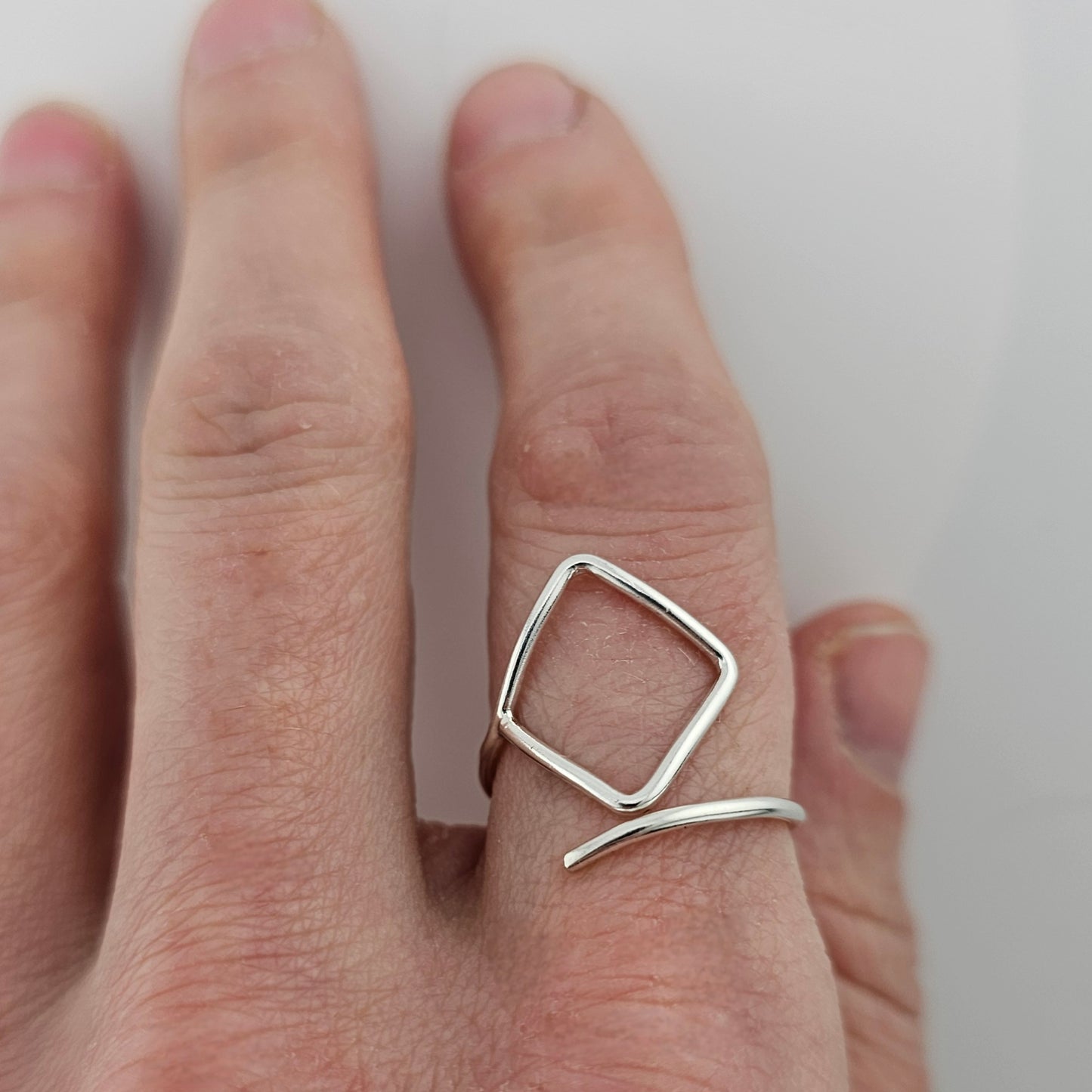 Woman's hand with silver square wire ring on pointer finger.