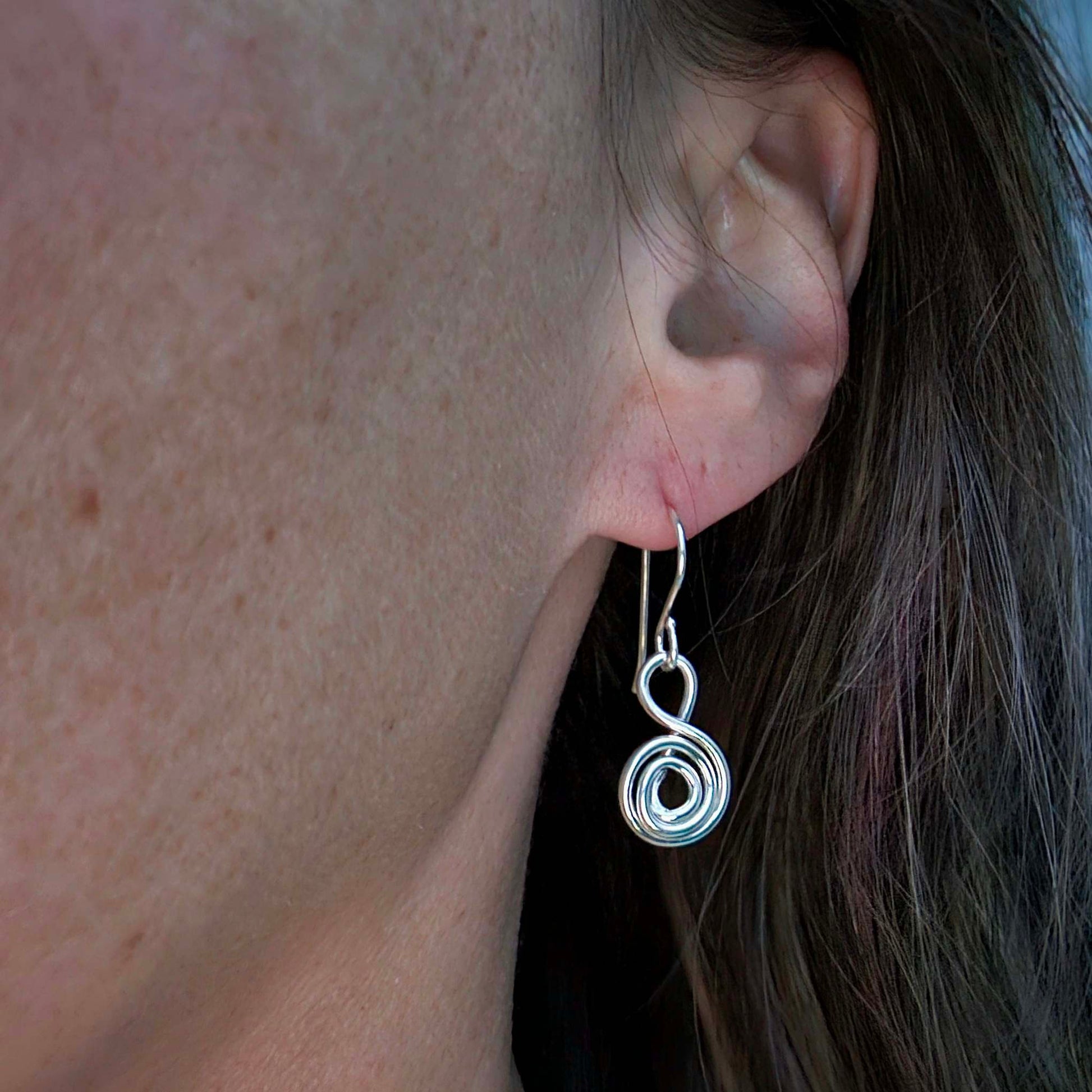 Drop silver Gratitude earrings worn on a woman's earlobe