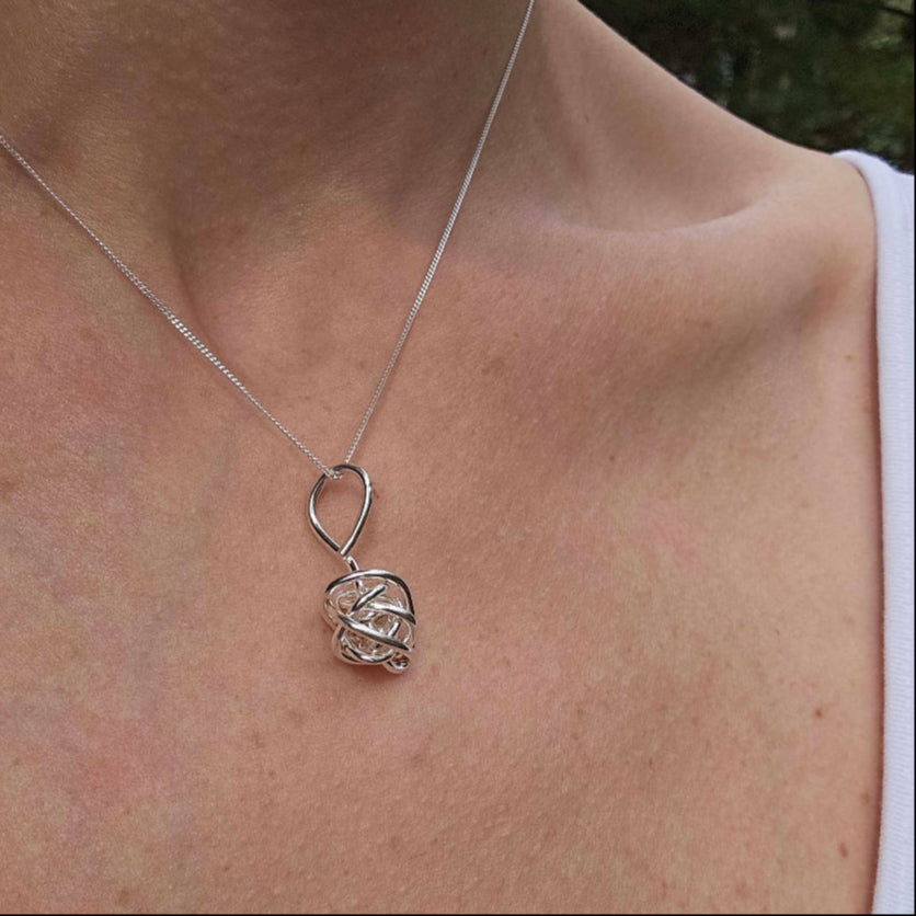 Silver Winding knot necklace worn around woman's neck by Jaclyn Nicole