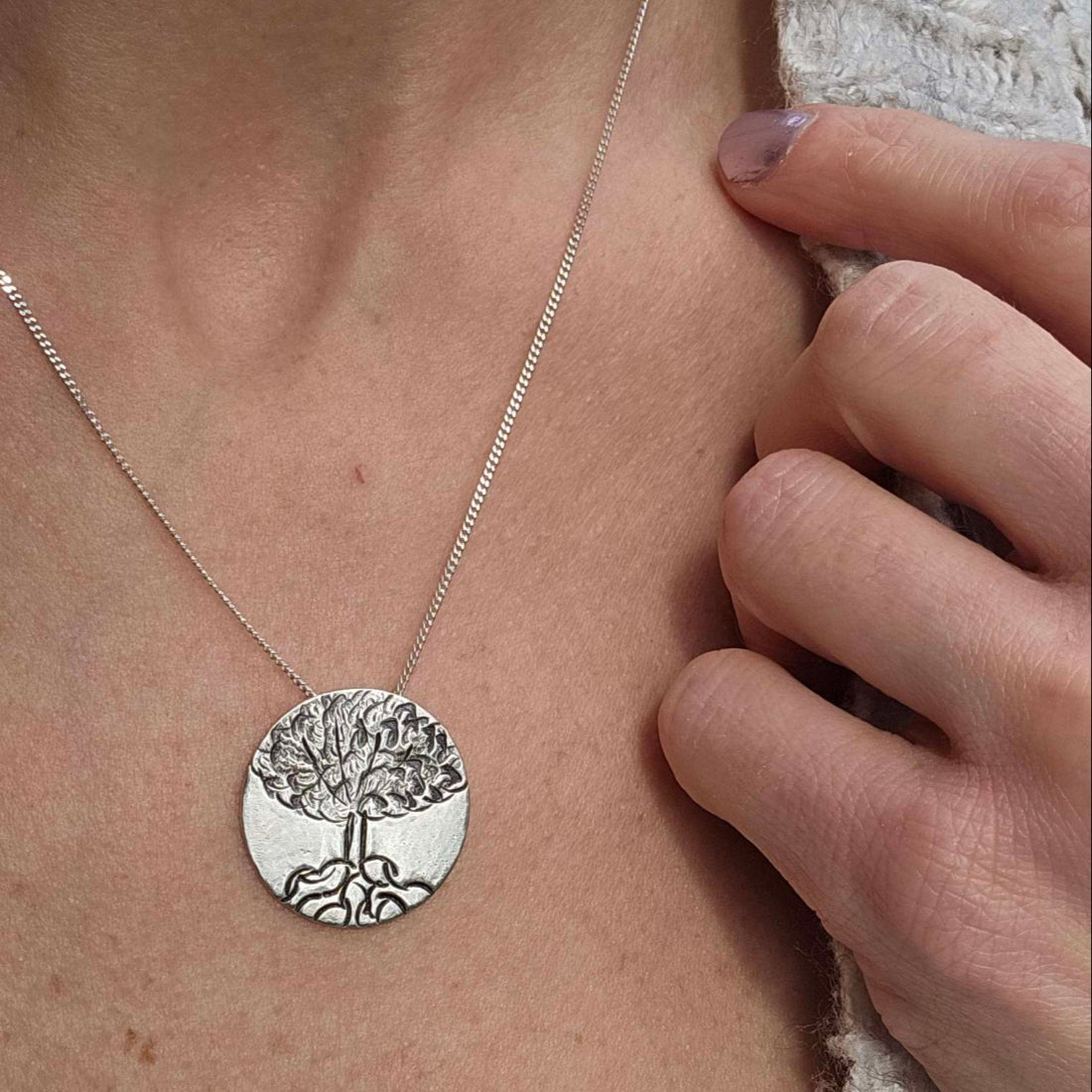 Sterling Silver Tree of Life Necklace worn on woman's neck with her hand grasping her sweater.