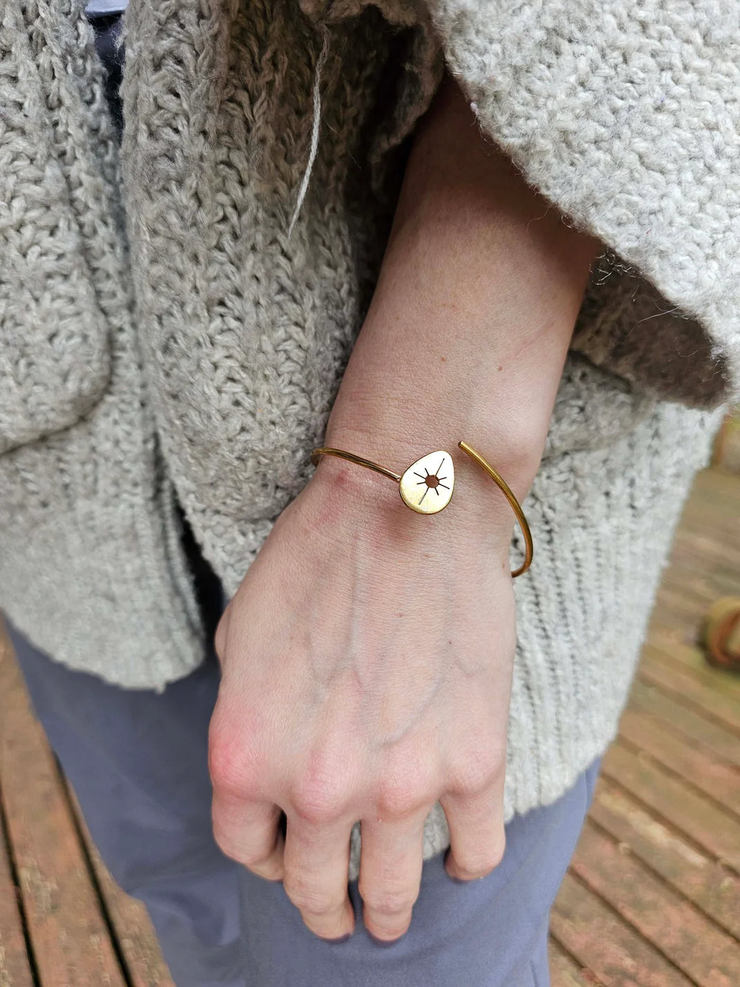 a person wearing a gold wrap bracelet with a sun symbol.