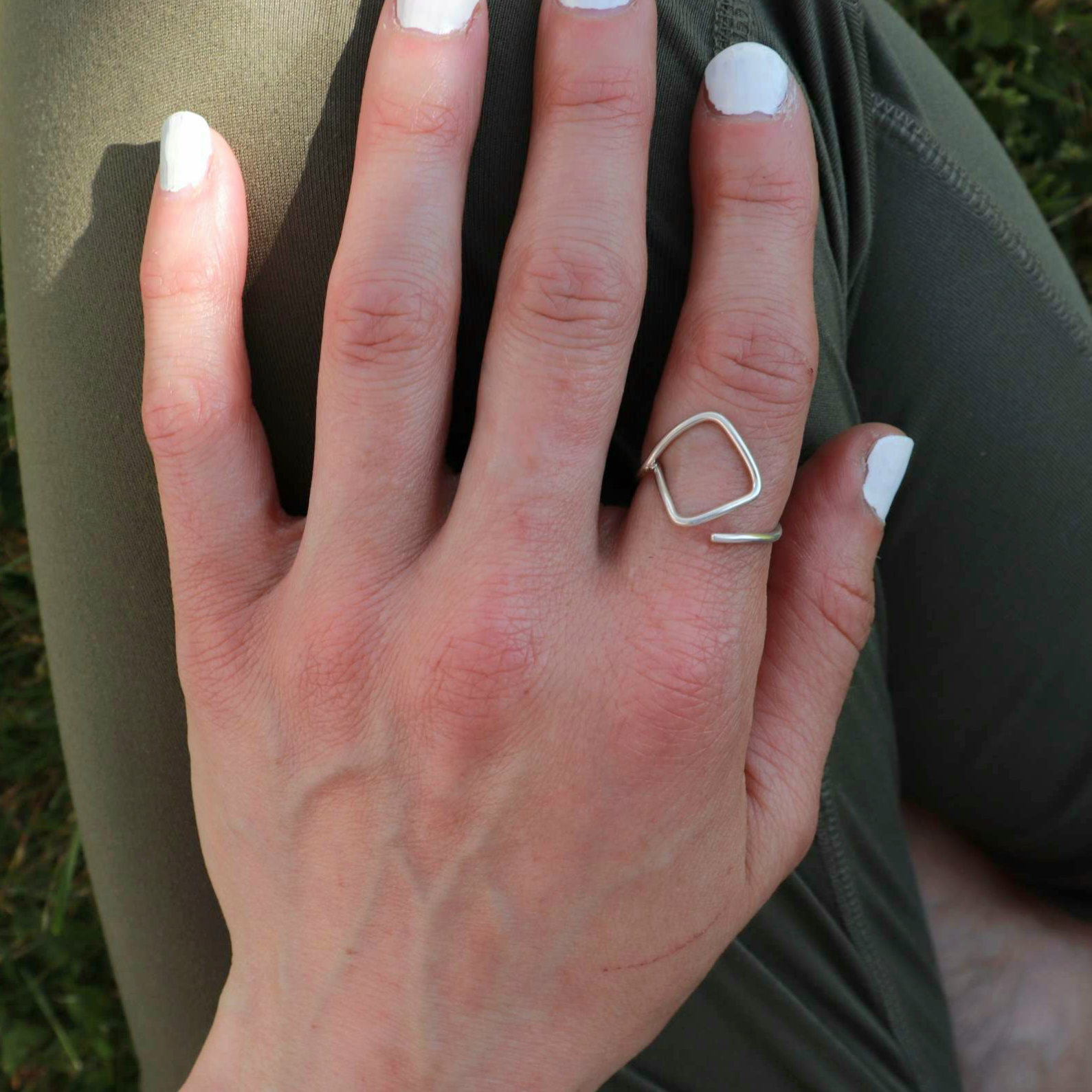 Silver ring worn on the pointer finger of a woman resting hand on legs wearing green pants.