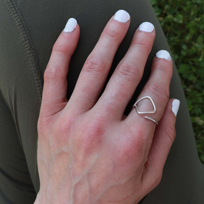 Silver ring worn on the pointer finger of a woman with white nail polish atop green pants.