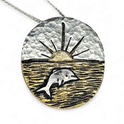 Silver and gold necklace pendant representing a sunset, ocean and silver dolphin.