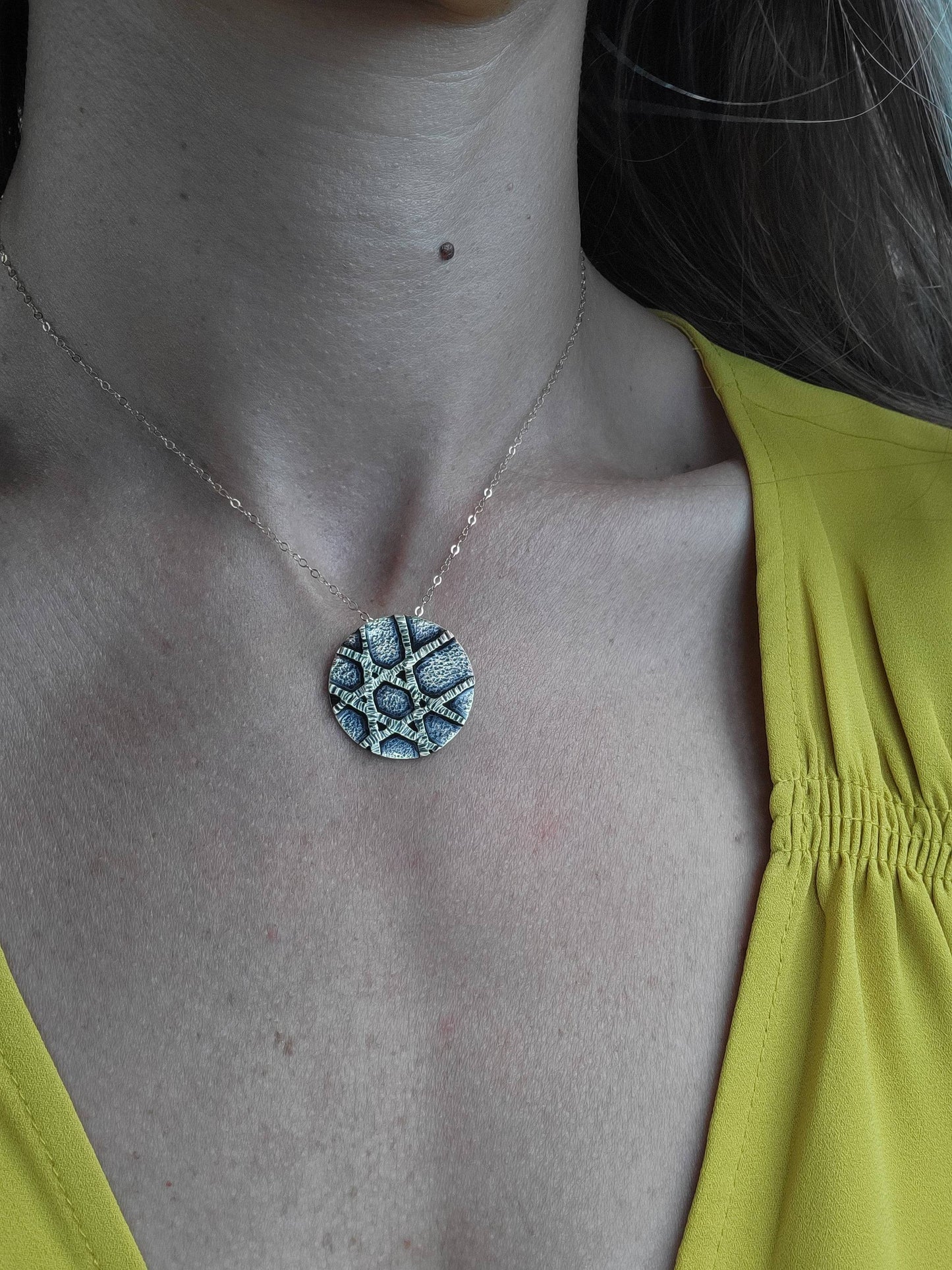 a woman in a yellow shirt and silver pendant necklace.